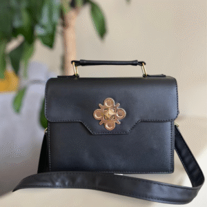 Bolso negro con herraje dorado en forma de talismán. Misterioso, protector y sofisticado: tu amuleto diario.